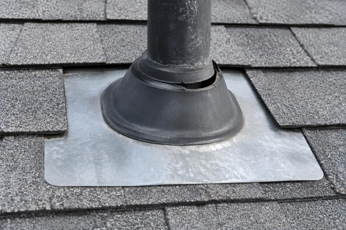 Split black rubber boot around a roof vent pipe above metal flashing and asphalt shingles